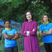 Woman in purple dress beside two people in blue t-shirts.