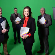Three men and a woman in front of a green screen.