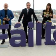 Two men and a woman standing behind a sign that says Failte with Dublin skyline in background.