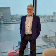 Man standing at window with port in background.