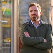 Man in green jumper with bus in background.