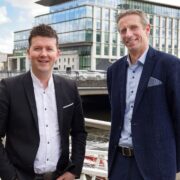 Two men standing beside a bridge.