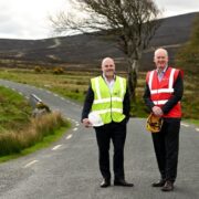 Two men on a country road wearing hi-vis jackets.