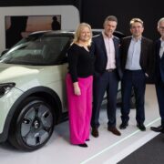 Three men and a woman in front of an electric vehicle.