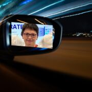 Woman inset on wing mirror of a truck on a highway at night.