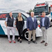 Three men and a woman standing in front of electric vehicles.