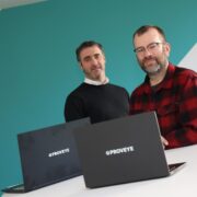 Two men standing behind two laptop computers.