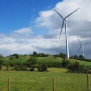 Wind turbines on a hill above green fields.