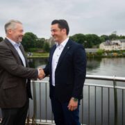 Two business men shake hands beside a river.