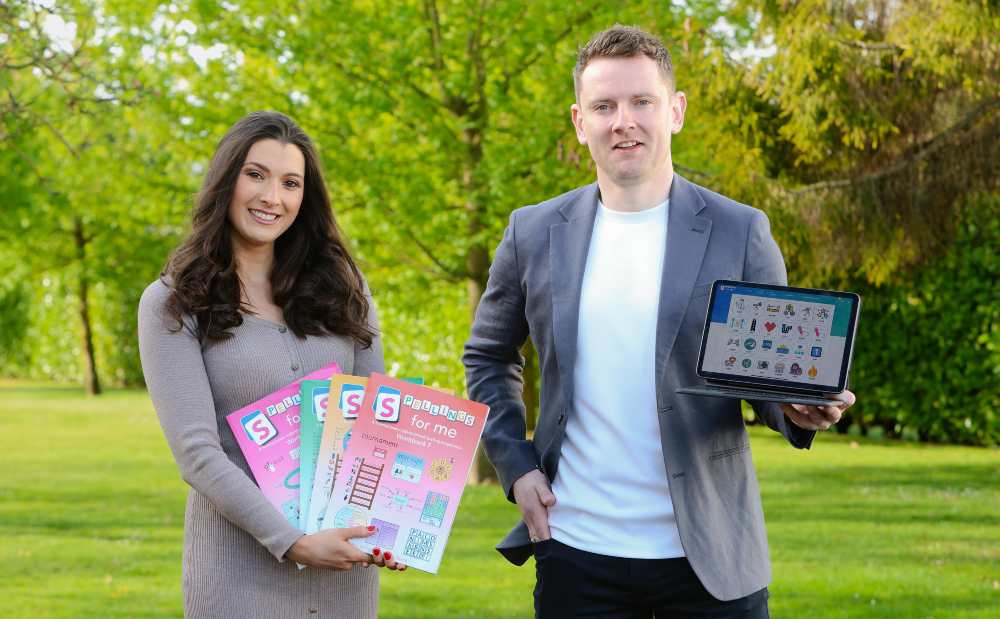 Man and woman holding a computer and learning materials.
