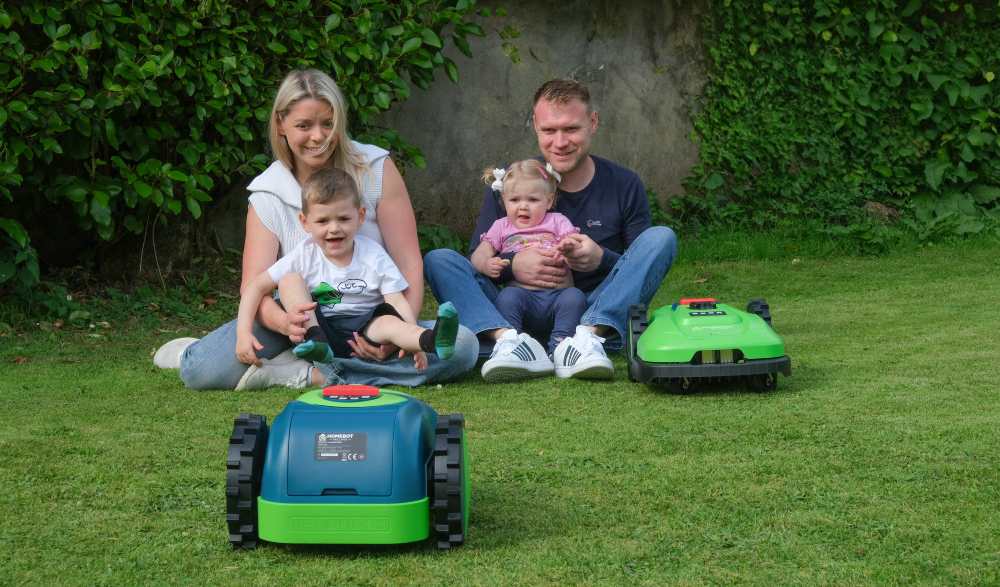 Mother and father with two children and two robot lawn mowers.