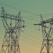 High-voltage electricity transmission towers and power lines silhouetted against a gradient sky at dusk.